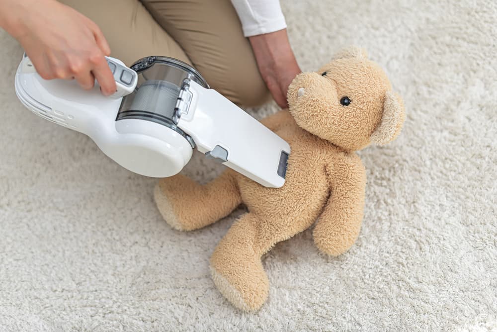 Cordless handheld vacuum cleaner being used to clean a teddy bear.