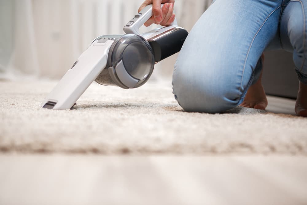 White cordless handheld vacuum cleaner being used to clean a carpet 