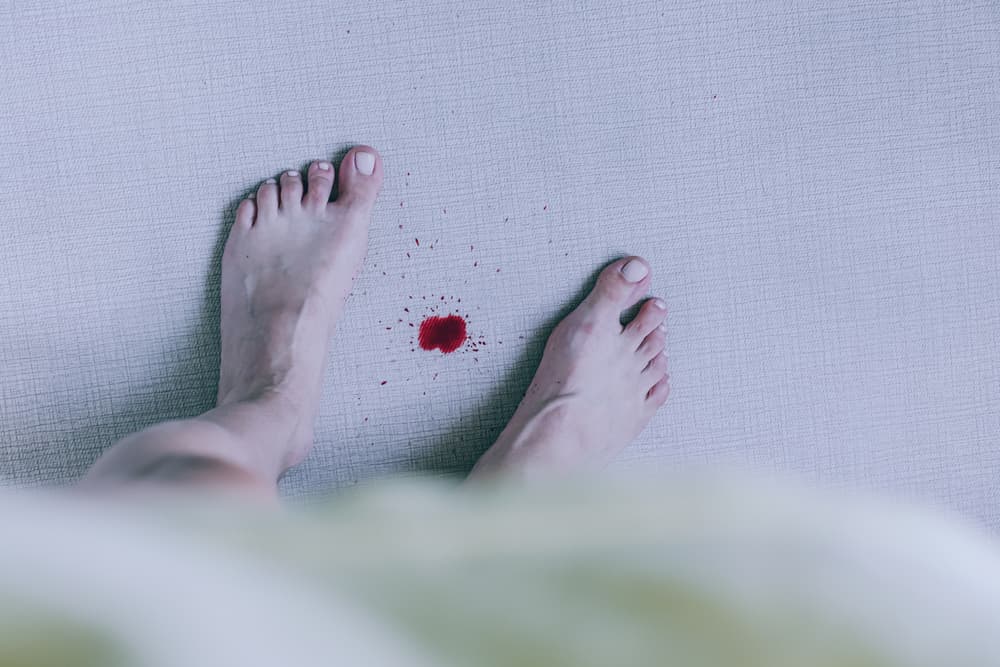 drop of blood on a white carpet between a woman's feet